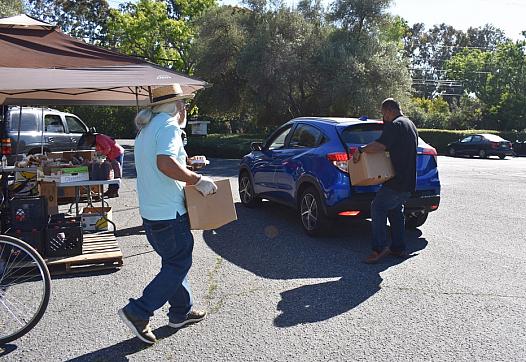Volunteers help load boxes of food into vehicles after asking drivers how many boxes of food they want on June 4, 2021