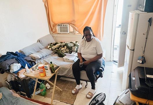 Kim Moore sits on her bed in a small unit of an unpermitted Mid-City apartment complex cited by the city in 2019.