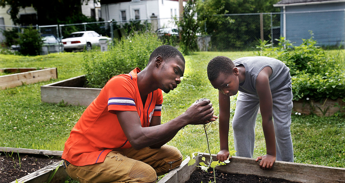 Nate Collins, 19, left, helps Deonta Williams, 9, prepare to plant a tomato plant on a Saturday in July at "We Got This," a prog