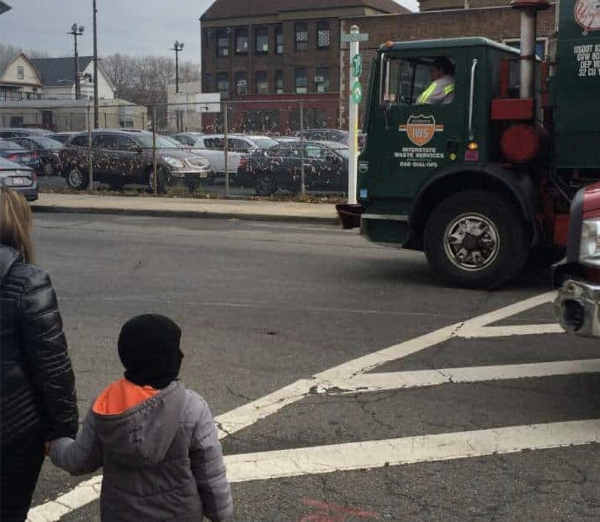 Trucks rumble along the road outside Hawkins Street School in Newark, New Jersey, as a family waits to cross.