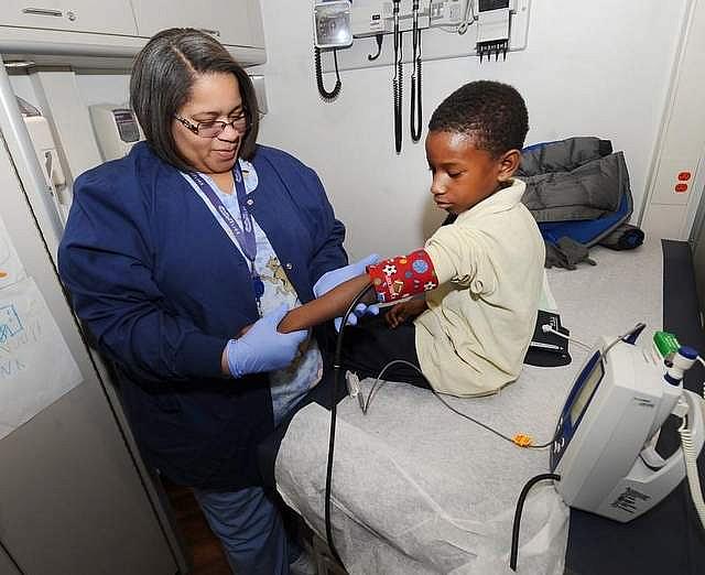 Tanisha Jones checks the blood pressure of Derrick Jenkins, 7, aboard a mobile clinic outside Dixon elementary school. (Photos by Max Ortiz / The Detroit News)  