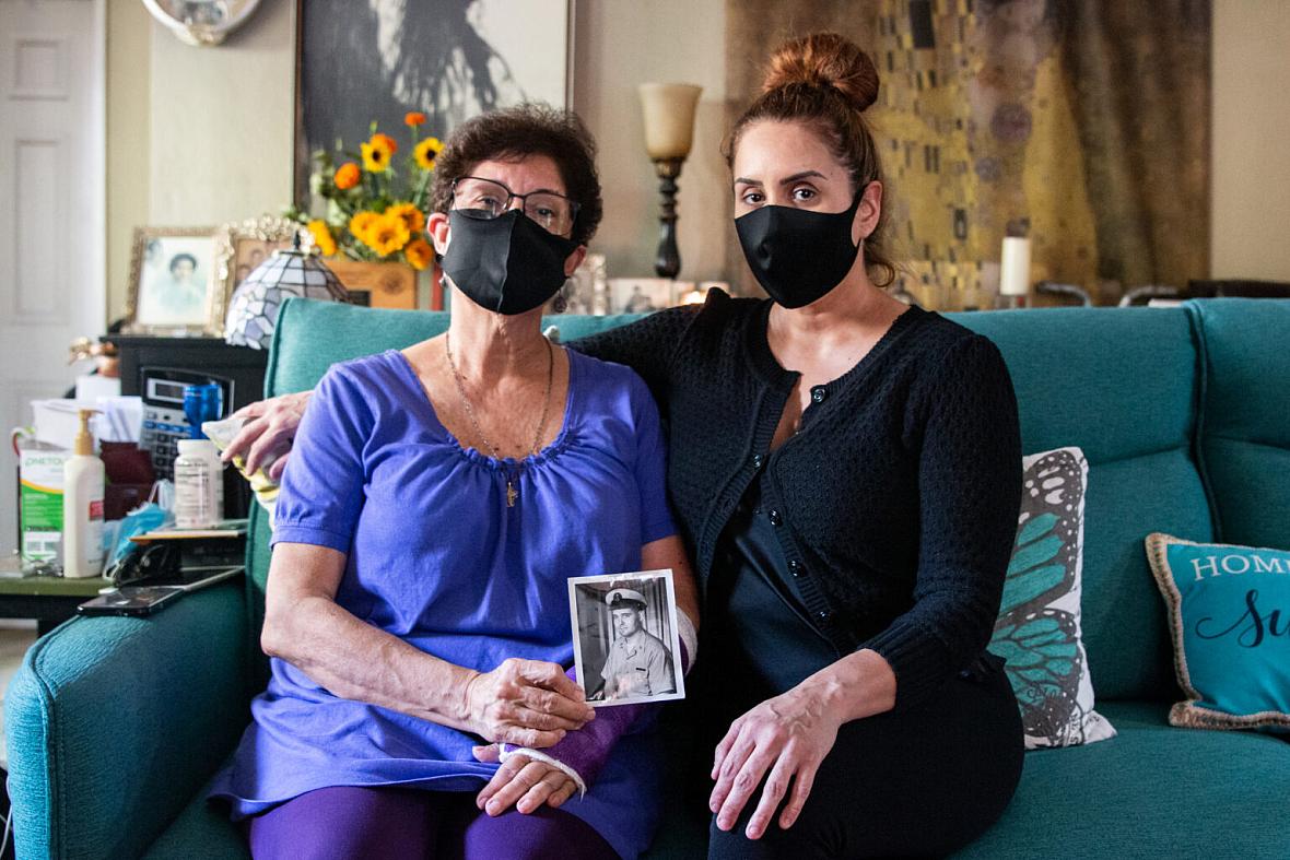 Elvia Sandoval and her daughter, Marcella Reed, pose with a photo of Reed’s grandfather, Walter Anderson, who contracted COVID-1