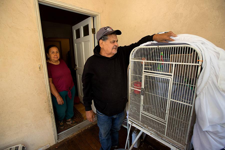  A man adjusts the cover on his parakeet cage as he and wife stand near the front of their home