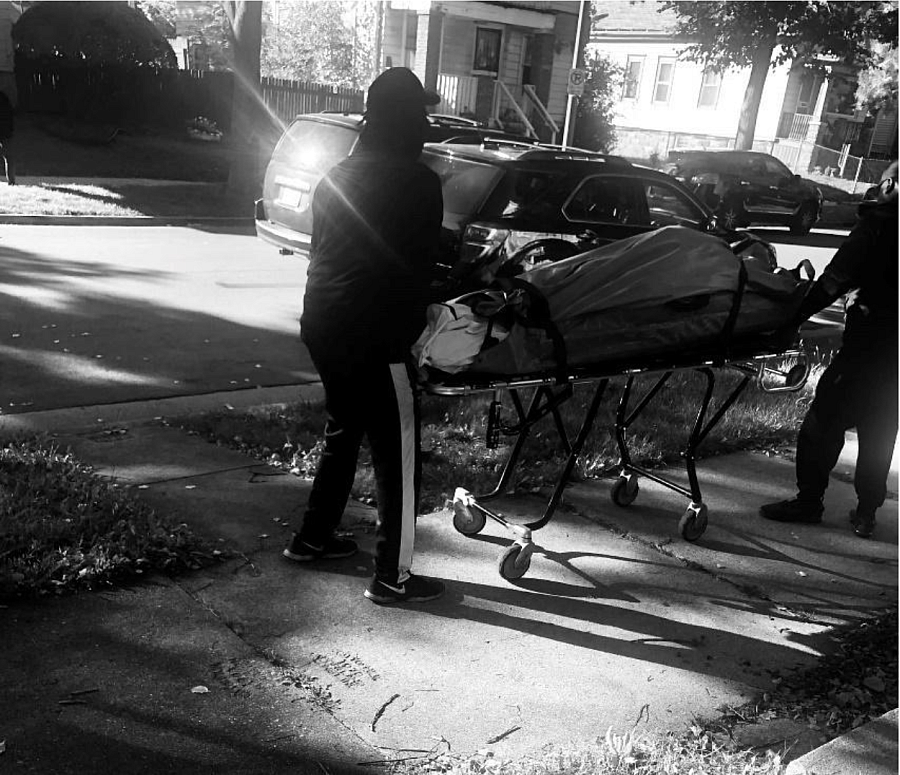 Black and white image of two people with Corpse on a stretcher.