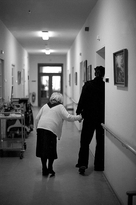 A person walking an old lady inside nursing home.