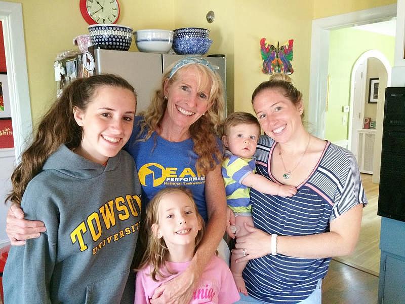 In the Colantuono's kitchen with two of Maya's biological children, Sophie (first from left) and Tori (right, holding her son), and Lana, in the pink shirt. Colantuonos fostered her as a baby but she was able to return to her mother. The Colantuonos are now her godparents, and Lana often stops by for a visit. Maya Colantuono is in the middle. Credit Kristin Gourlay / RIPR