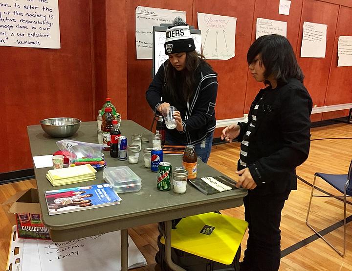 Two volunteers scoop sugar into jars to see how much is included in popular beverages. Two volunteers scoop sugar into jars to see how much is included in popular beverages.