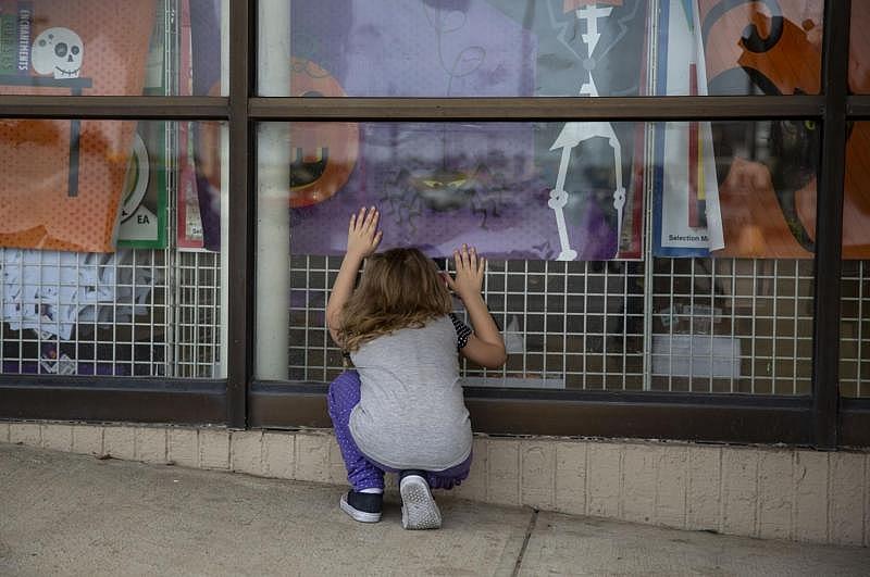 Zoey looks at Halloween decorations through the window of Dollar Tree while her mother and sister attempt to collect enough donation money to rent a motel room for the night.