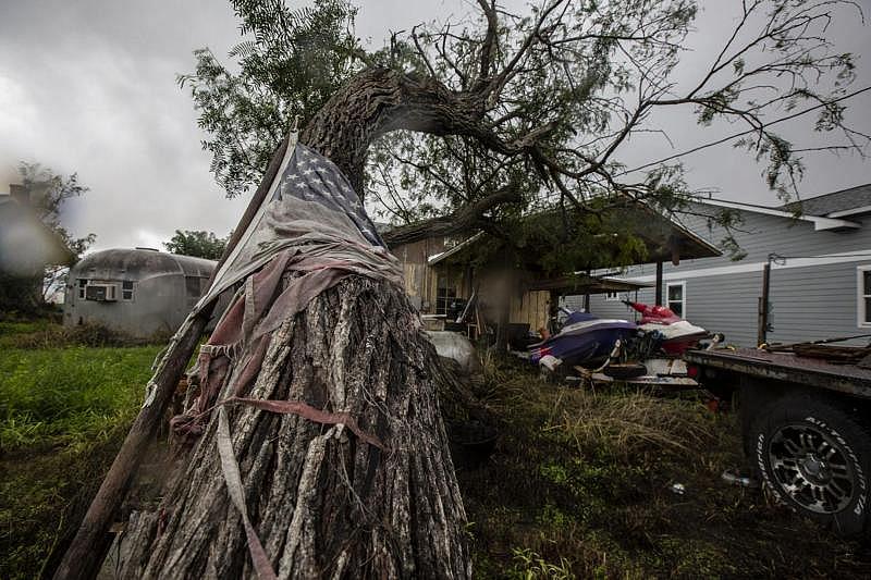 A faded, shredded American flag is wrapped around a tree in front of a waterfront property on Copano Bay Drive from which a family fled after Harvey damaged it. A newly built house towers over the home. (Photo Credit: Angela Piazza/Victoria Advocate) A faded, shredded American flag is wrapped around a tree in front of a waterfront property on Copano Bay Drive from which a family fled after Harvey damaged it. A newly built house towers over the home.