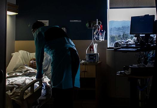 A patient lies in a hospital bed, with a health care provider attending.