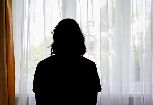 A woman is silhouetted against a window curtain.
