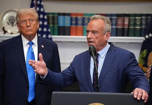 RFK Jr. stands before a podium, with President Trump behind him, at a White House press conference.