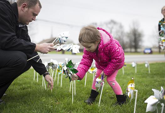 Elizabeth Crouch, 4, (center) places pinwheels in the ground with Det. Adam Corbett 